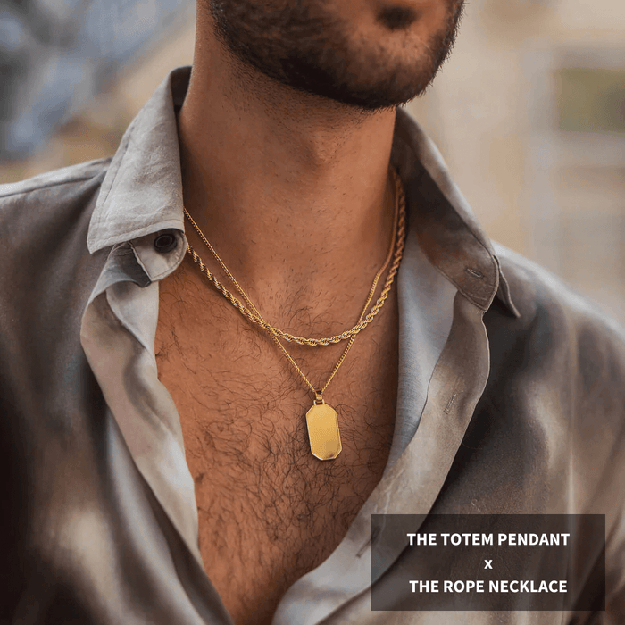 Man wearing two gold necklaces layered over a partially unbuttoned gray shirt, featuring a bold Totem pendant and a thick rope chain in the Build Your Own Bundle - Gold collection.