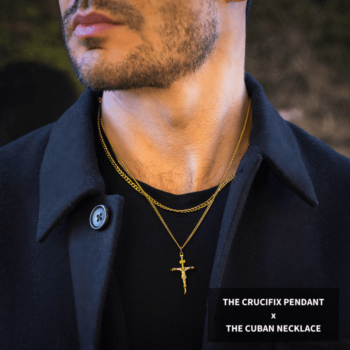 Close-up of a man wearing The Crucifix Essentials Bundle - Gold featuring a gold crucifix pendant and a matching gold Cuban necklace layered over a black shirt and dark coat, showcasing bold men's jewelry.