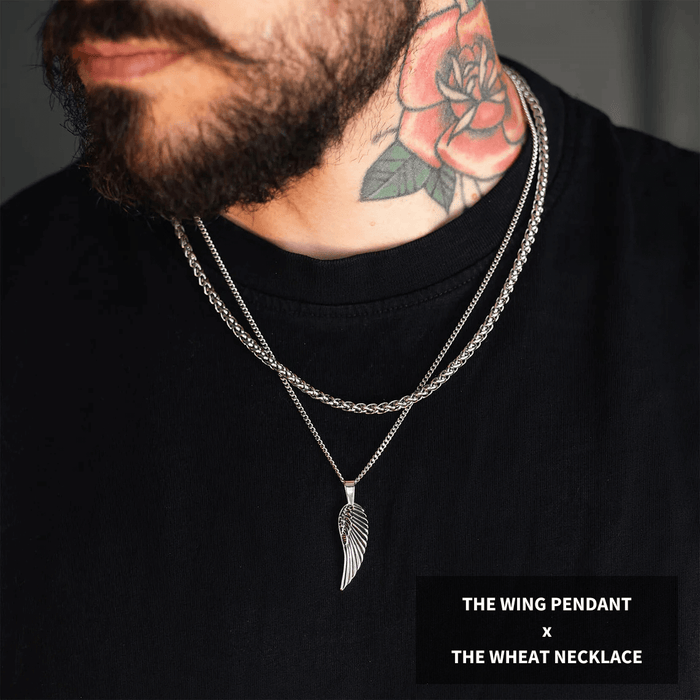 Man wearing two silver chains layered over a black shirt featuring a wing-shaped pendant and a wheat-inspired necklace from the Build Your Own Bundle - Silver collection, styled boldly by Ralph Christian.