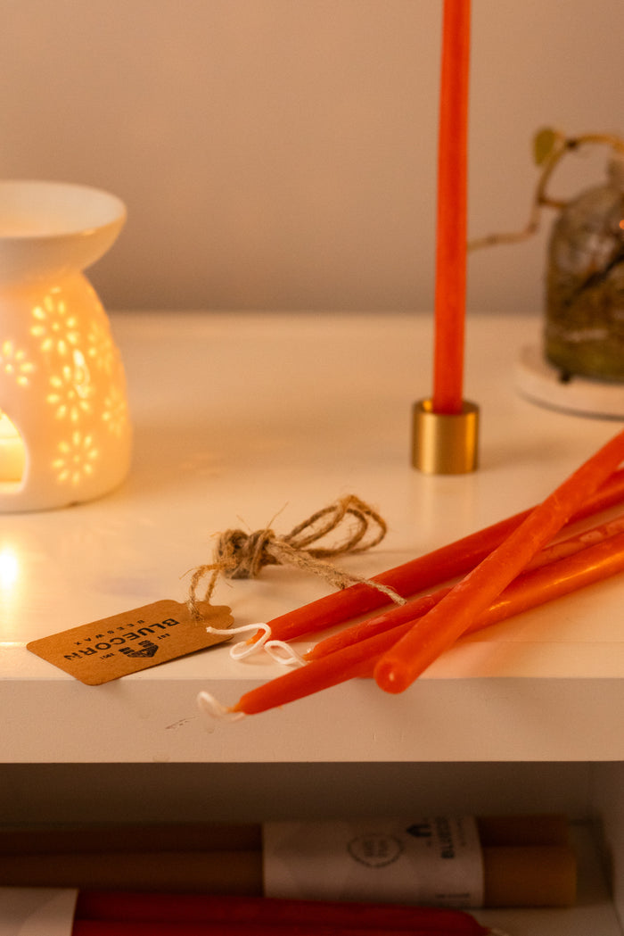 An Apricot beeswax hand dipped thin beeswax taper in a brass taper holder next to an opened bundle of Apricot Thin Beeswax tapers with other decorative items