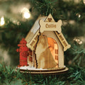 A wooden Christmas ornament shaped like a doghouse with a bone-shaped sign that says Collie, a red fire hydrant, and a silhouette of a collie, hanging on a green Christmas tree.