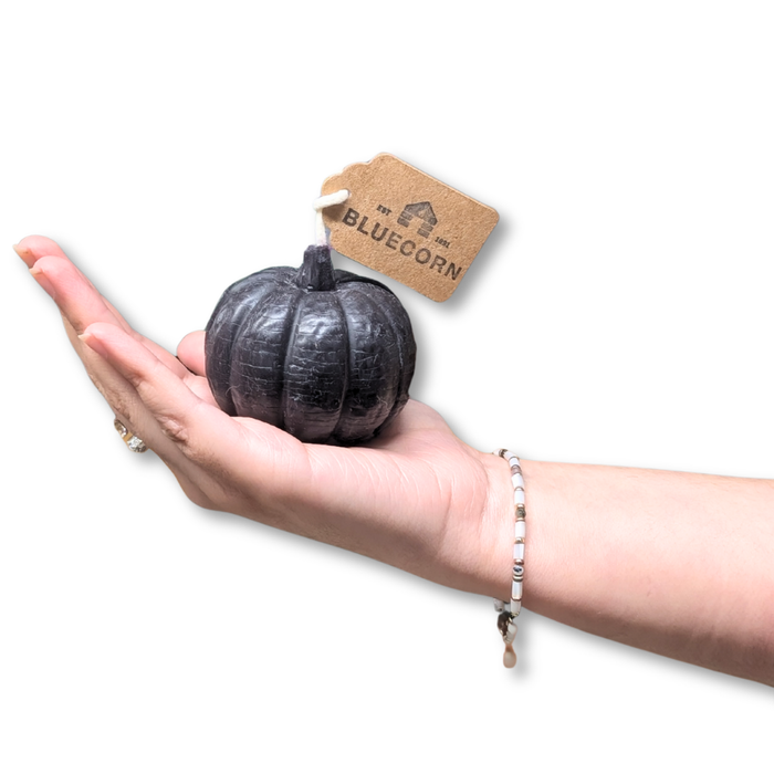 A hand holding a black pumpkin shaped candle with a tag, showcasing the unique design.
