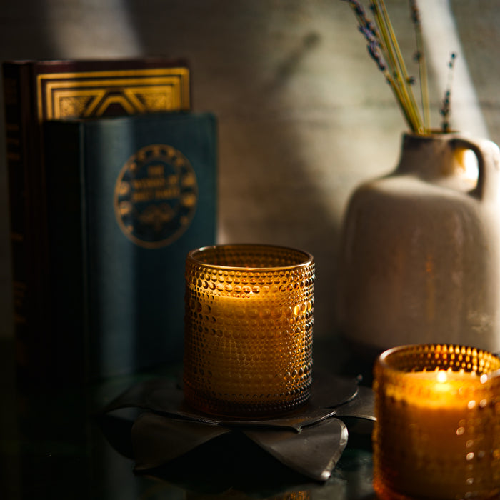 Winter scented candle glowing softly beside a book and vase, creating a cozy ambiance.