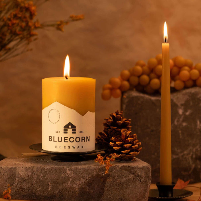 Hand-dipped beeswax taper candles and a beeswax pillar candle with a warm glow on stone surfaces.