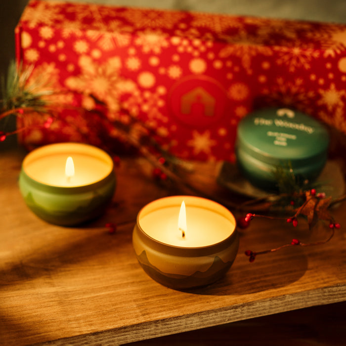 Scented candle gift set featuring two lit tins and a festive red box with snowflakes.