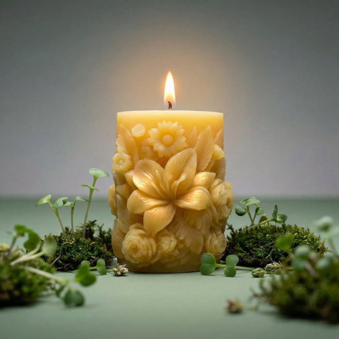 Decorative beeswax pillar candle with floral patterns surrounded by greenery on a neutral background