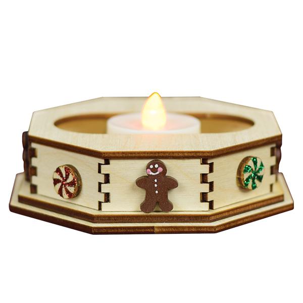 A wooden octagonal candle holder decorated with a gingerbread man, red and green peppermint candies, and a flickering LED tealight in the center.
