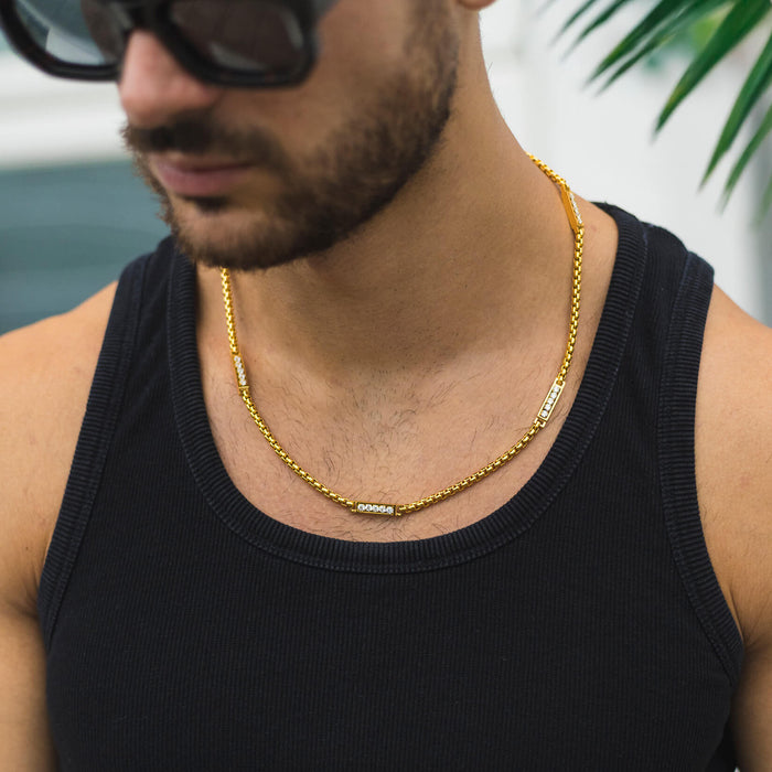 Man wearing The Atlas Ice Necklace, a bold men's jewelry piece featuring a gold-tone chain with cubic zirconia accents, styled with a black tank top and sunglasses.