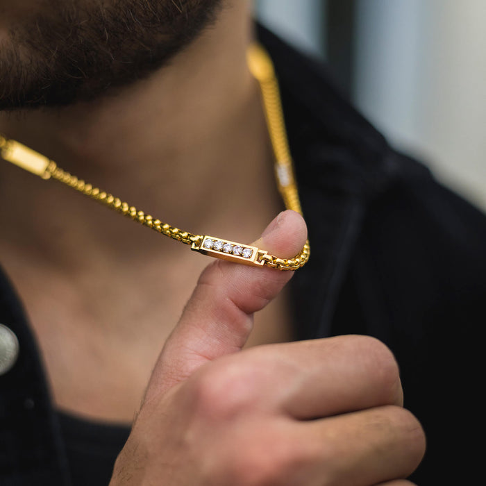 Close-up lifestyle shot of a man holding the gold chain of The Atlas Ice Necklace featuring cubic zirconia accents, showcasing bold men's jewelry with a standout design.