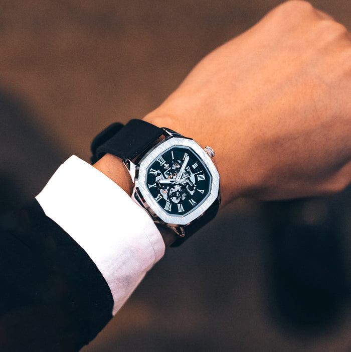 The Avalon - Silver men's luxury watch features a polished silver case with intricate dial details, Roman numeral markers, and a black strap in an elegant on-wrist lifestyle shot.