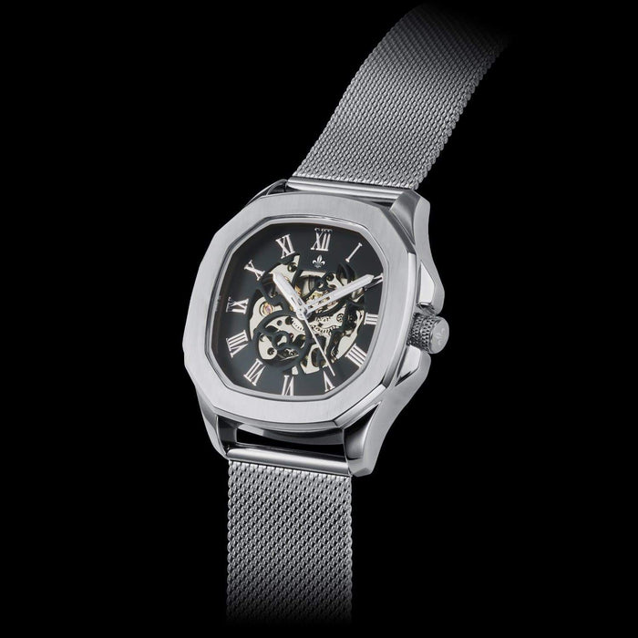 The Avalon - Silver men's luxury watch featuring a silver mesh bracelet, angular polished case, black dial with Roman numerals, skeleton design, and intricate watchmaking detail. Bold by Design.