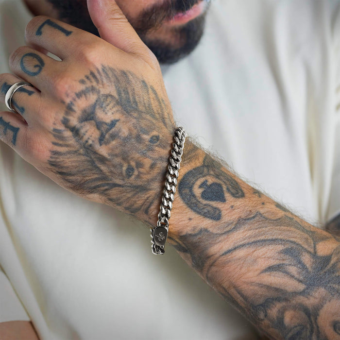 Close-up lifestyle image of a man wearing The Cuban Bracelet - Silver, a bold silver chain bracelet that complements his detailed lion and script tattoos, embodying statement luxury jewelry bold by design.