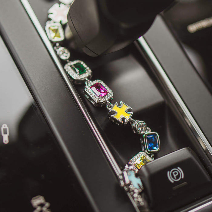 The Gemstone Bracelet displayed on a sleek black surface with multicolored cubic zirconia stones set in silver links, featuring bold, standout design with a mix of rectangular and geometric shapes.