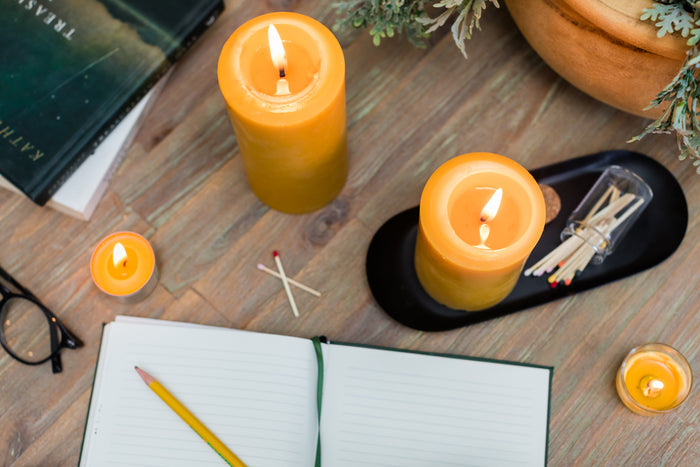Raw beeswax pillar candles on a wooden surface with matches and a notebook.