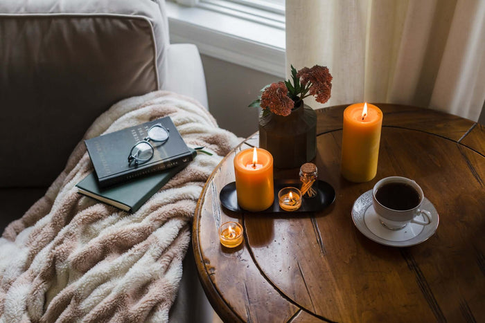 Beeswax pillar candles in candlelit scene with a book, glasses, flowers, and coffee on a wooden table.