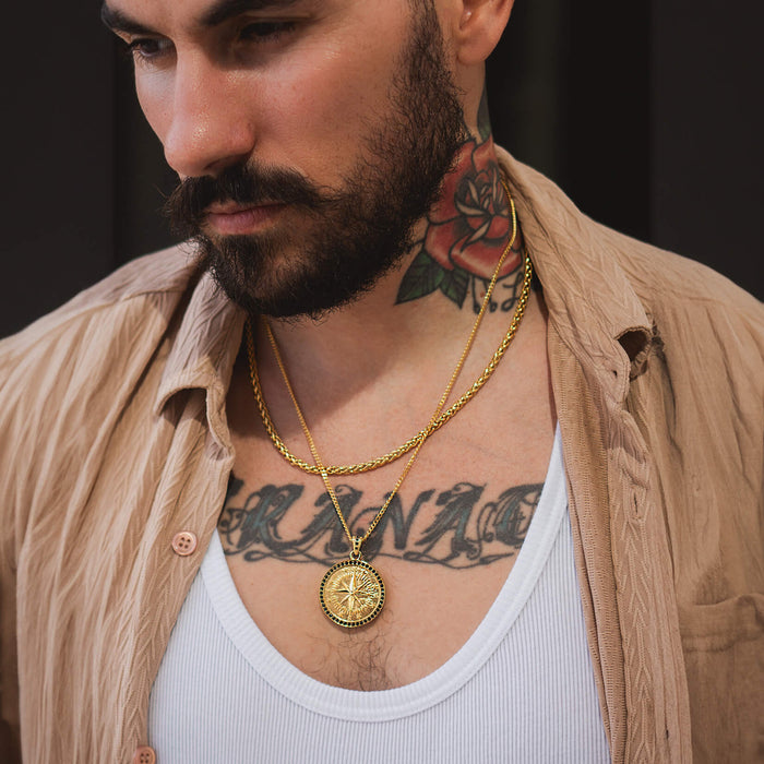 Man wearing layered gold chains featuring The Gold Compass Pendant - Essentials Collection, styled with a beige shirt and white tank top, showcasing bold men's jewelry.