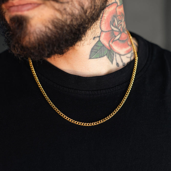 Close-up of a male model wearing The Gold Cuban Necklace - Essentials Collection, featuring a bold gold chain design styled with a black shirt and visible neck tattoo.