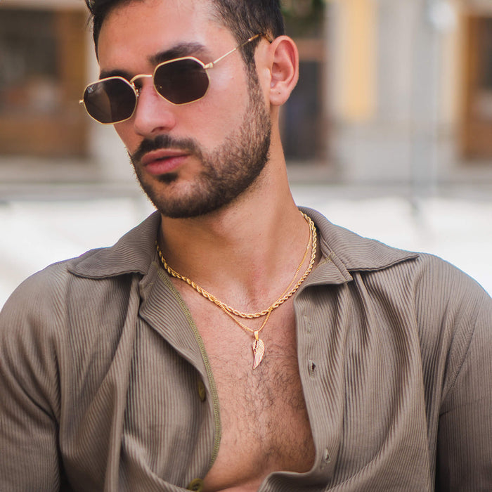 Man wearing stylish sunglasses and an open-collar textured shirt, showcasing The Gold Wing Pendant - Essentials Collection, a bold men’s jewelry piece with a gold wing-shaped charm on a matching gold chain.