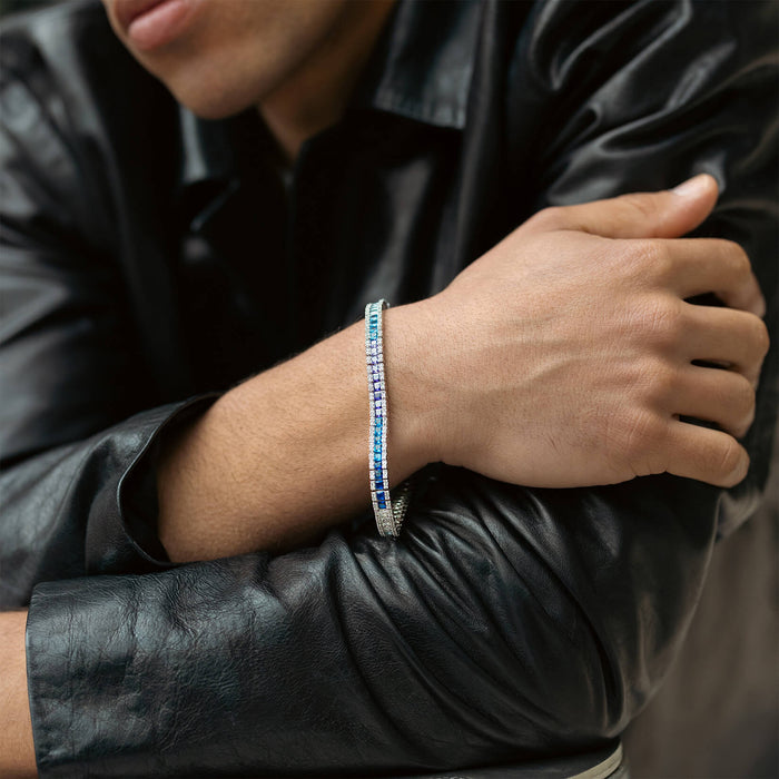 A close-up of a man's wrist wearing The Iced Atlantis Bracelet, featuring a sleek silver-toned design with alternating blue and clear cubic zirconia stones, styled with a black leather jacket.