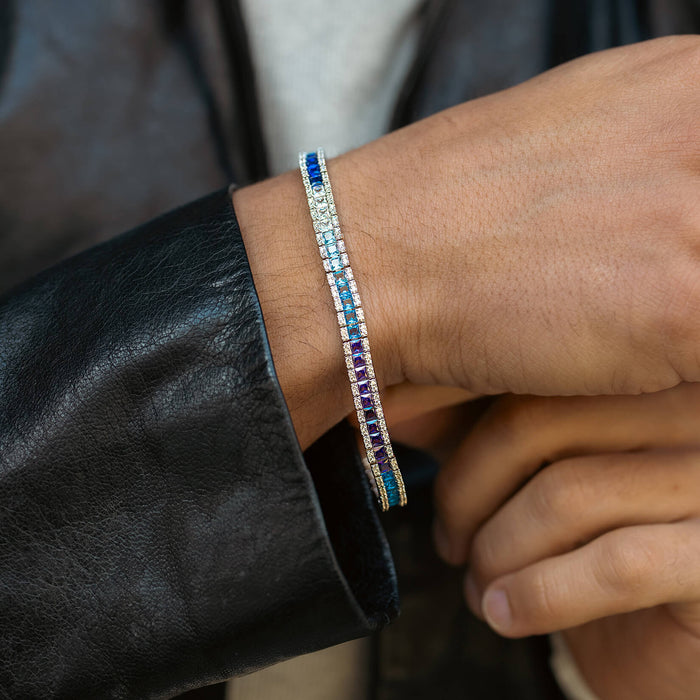 The Iced Atlantis Bracelet on a male wrist featuring a slim, multi-colored cubic zirconia design with bold blues, purples, and clear stones, styled with a black leather jacket sleeve.