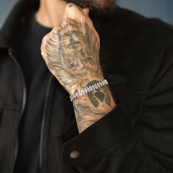 A close-up of a male wrist wearing The Iced Creed Bracelet - Silver, featuring a bold silver link design that complements detailed hand tattoos and a black jacket sleeve.