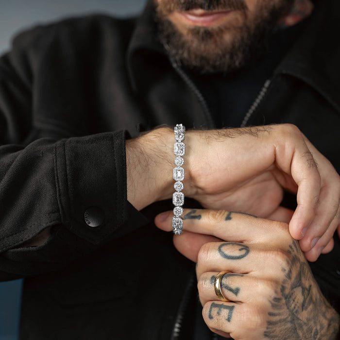 A man wearing a black jacket showcasing The Iced Versailles Bracelet, a bold men's jewelry piece featuring large, clear cubic zirconia stones set in a silver-tone metal chain.