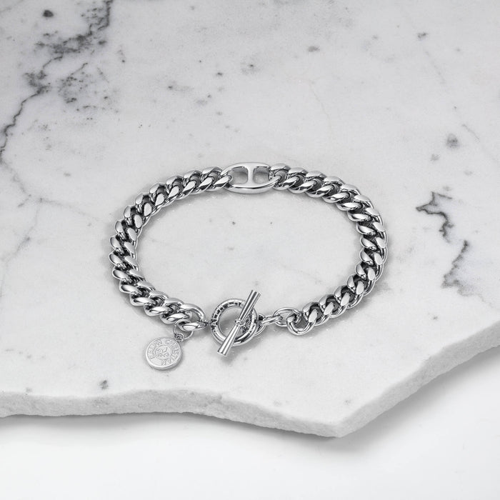 The Medallion Bracelet - Silver displayed on a white marble surface, featuring a bold silver chain link design with a toggle clasp and a small engraved medallion charm, bold by design.