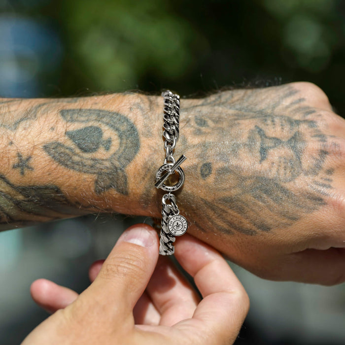 The Medallion Bracelet - Silver on a tattooed wrist, featuring a chunky silver chain and a round medallion charm with a toggle clasp, styled in natural light.