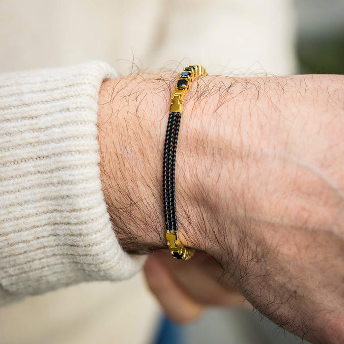 Close-up of a man's wrist wearing The Midnight Luxe Bracelet featuring a black woven band with gold-tone accents, showcasing a bold by design men's jewelry statement.