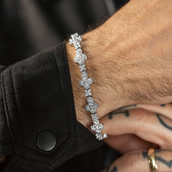 Close-up of a wrist wearing a silver-toned bracelet with multiple clover-shaped links adorned with sparkling cubic zirconia stones, styled with a black jacket cuff.