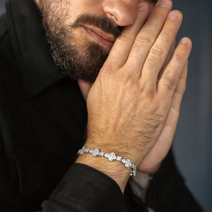 Close-up of a man's wrist wearing a silver bracelet with multiple linked flower-shaped cubic zirconia accents against a dark shirt background, styled for a bold statement look.