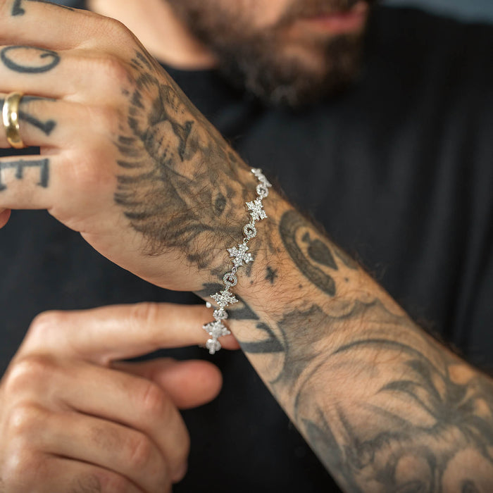 A close-up of a male wrist adorned with The Orion Iced Bracelet featuring sparkling cubic zirconia stones in a unique flake design, complementing bold tattooed skin.