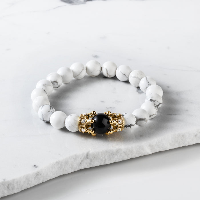 The Royal Howlite Bracelet featuring smooth white howlite beads with subtle gray veining, accented by a central black bead capped with ornate gold crowns, bold by design.