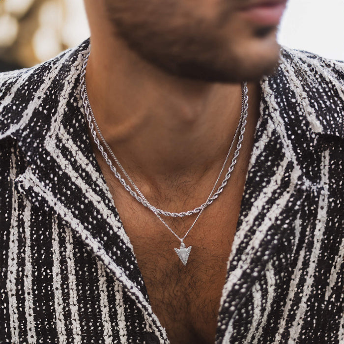 Close-up of a man wearing The Silver Rope Necklace - Essentials Collection, featuring a bold silver rope chain and a geometric arrow pendant, styled with a textured black and white jacket, embodying statement men's jewelry Bold by Design.