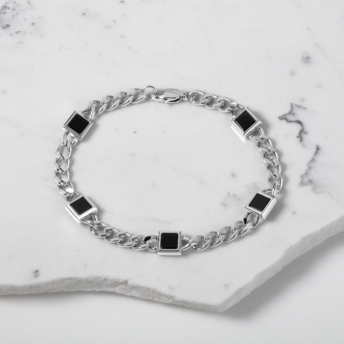 The Urban Agate Bracelet featuring a men's silver chain link design with five polished black square onyx accents, presented on a white marble surface.