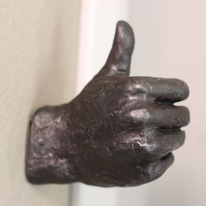 Bronze hand sculpture giving a thumbs-up gesture on a plain background