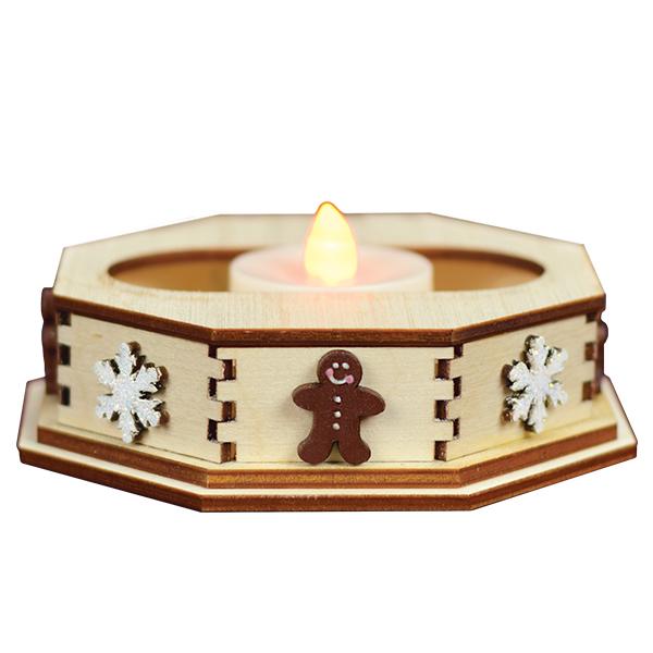 A wooden octagonal candle holder decorated with white snowflakes and a gingerbread man, holding a lit tealight candle.